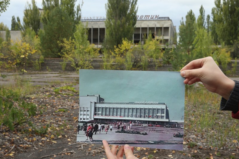 PRIPYAT, UKRAINE - SEPTEMBER 29: An assistant holds up a photo showing the city of Pripyat's main square and the "Energetik" cultural center before 1986 at the same site that today is abandoned and overgrown with trees on September 29, 2015 in Pripyat, Ukraine. Pripyat lies only a few kilometers from the former Chernobyl nuclear power plant and was built in the 1970s to house the plant's workers and their families. On April 26, 1986, technicians at Chernobyl conducting a test inadvertently caused reactor number four to explode, sending plumes of highly radioactive particles and debris into the atmosphere. Authorities evacuated 120,000 people from the area, including 43,000 from Pripyat. Today Pripyat is a ghost-town, its apartment buildings, shops, restaurants, hospital, schools, cultural center and sports facilities derelict and its streets overgrown with trees. The city lies in the inner exclusion zone around Chernobyl where hot spots of persistently high levels of radiation make the area uninhabitable for thousands of years to come. (Photo by Sean Gallup/Getty Images)