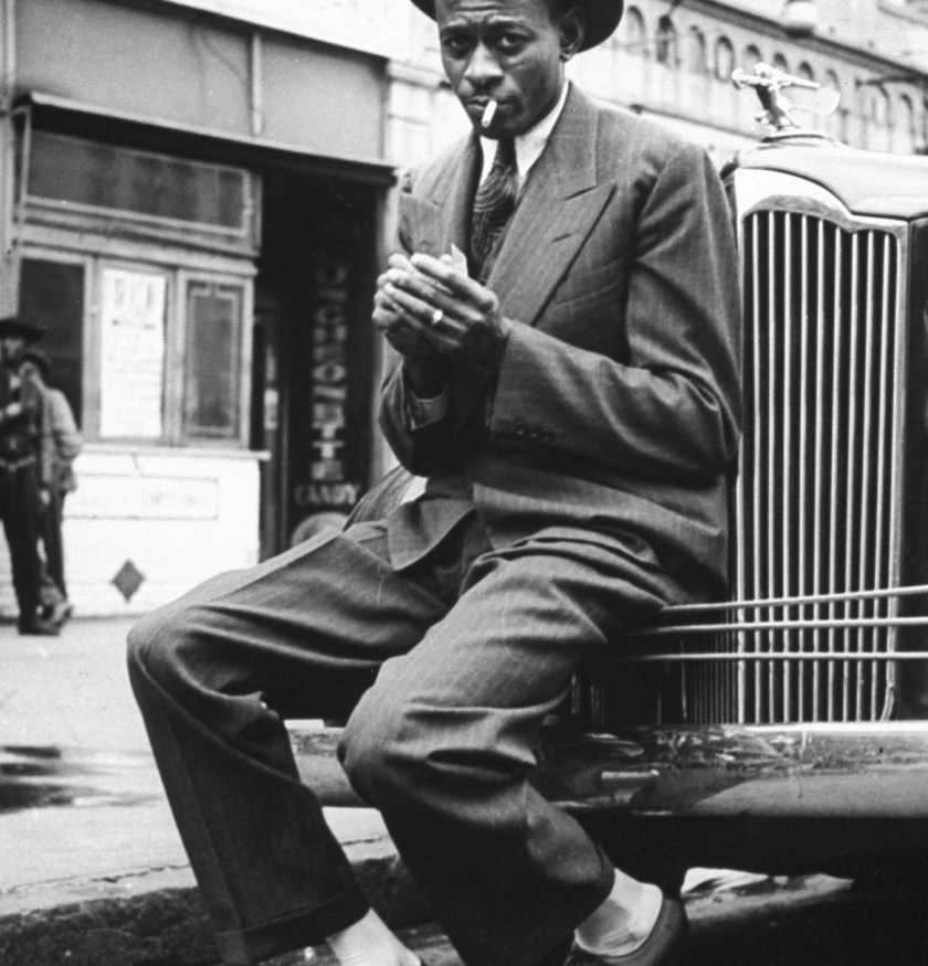 Baseball player Satchel Paige, looking dapper, lighting his cigarette while sitting on front bumper of large car. (Photo by George Strock/The LIFE Picture Collection/Getty Images)