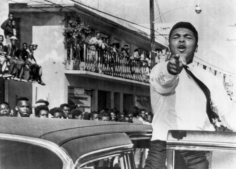 American boxer Cassius Clay (later known as Muhammad Ali) points at the camera from an open car door as he takes part in a pre-football game parade, Miami, Florida, December 14, 1963. He was Miami to train for his title fight against Sonny Liston. (Photo by Underwood Archives/Getty Images)