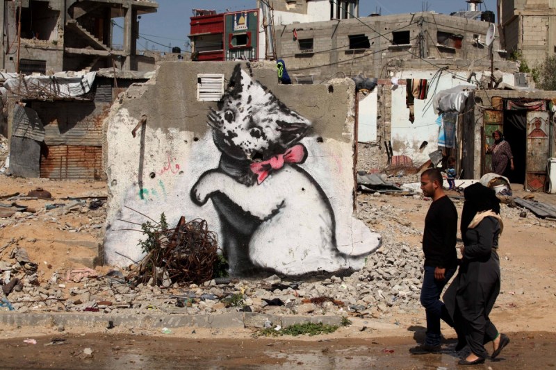 BEIT HANOUN, GAZA - FEBRUARY 27: People pass by a graffiti on a wall of a building drawn by British artist Banksy in Beit Hanoun, Gaza on February 27, 2015. Famous British artist Banksy visited Gaza and drew graffiti on the walls of houses in Beit Hanoun destroyed in Israel's recent attacks on Gaza. (Photo by Ashraf Amra/Anadolu Agency/Getty Images)