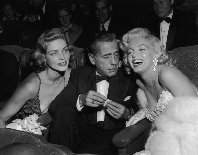 1953: EXCLUSIVE Married American actors Lauren Bacall (L) and Humphrey Bogart (1899 - 1957) pose with American actor Marilyn Monroe (1926 - 1962) at the premiere of director Jean Negulesco's film, 'How to Marry a Millionaire'. Bacall and Monroe costarred in the film. (Photo by Darlene Hammond/Hulton Archive/Getty Images)