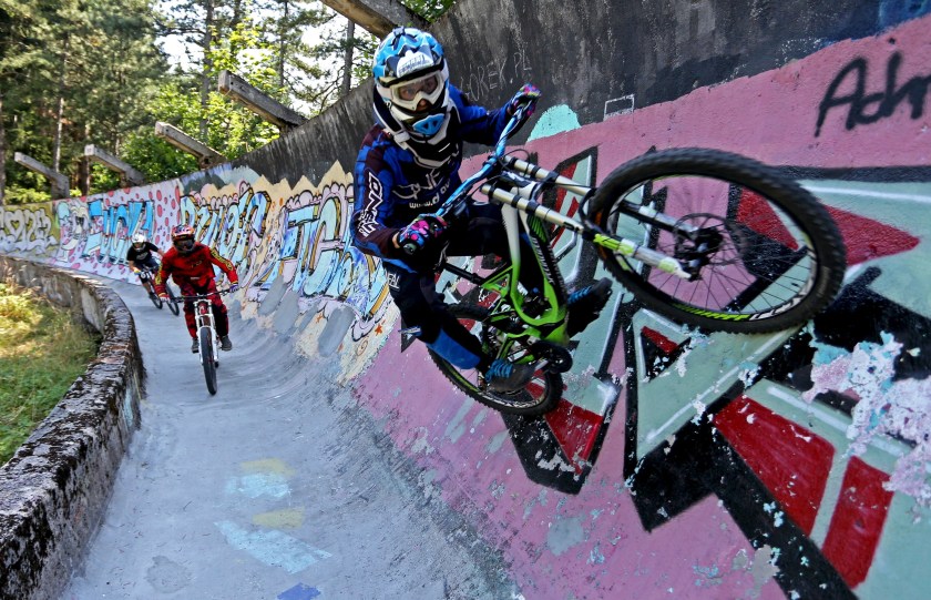 Downhill bikers Kemal Mulic (C), Tarik Hadzic (L) and Kamer Kolar train on the disused bobsled track from the 1984 Sarajevo Winter Olympics on Trebevic mountain near Sarajevo, Bosnia and Herzegovina, August 8, 2015. Abandoned and left to crumble into oblivion, most of the 1984 Winter Olympic venues in Bosnia's capital Sarajevo have been reduced to rubble by neglect as much as the 1990s conflict that tore apart the former Yugoslavia. The bobsled and luge track at Mount Trebevic, the Mount Igman ski jumping course and accompanying infrastructure are now decomposing into obscurity. The bobsled and luge track, which was also used for World Cup competitions after the Olympics, became a Bosnian-Serb artillery stronghold during the war and is nowadays a target of frequent vandalism. Picture taken August 8. REUTERS/Dado Ruvic TPX IMAGES OF THE DAY - RTX1NQ1L