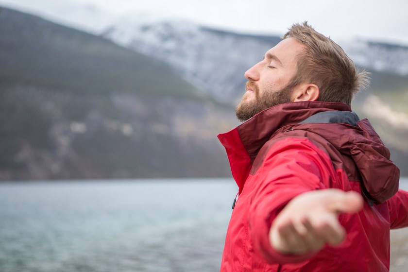 Young cheerful man by the lake arms outstretched for positive emotion.