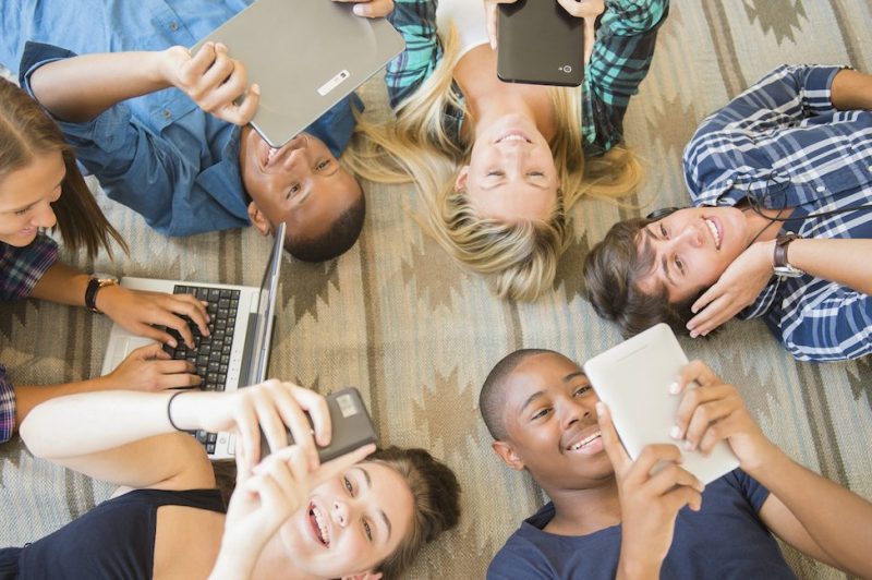 Teenagers laying on floor using technology