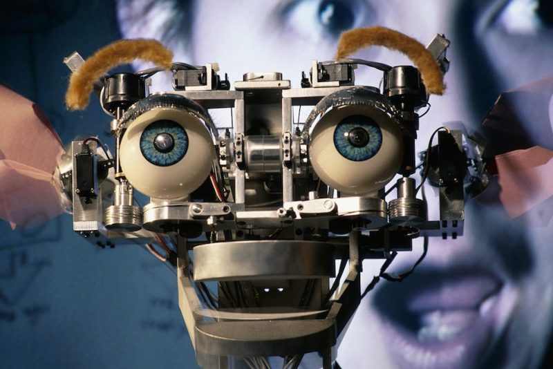 Kismet is the expressive robot built by Cynthia Breazeal at M.I.T.'s Artificial Intelligence Lab. Kismet can engage humans in simple social interactions, hopefully leading to communication with human caregivers using infant-like expressions and vocalizations. Here it shows a surprise reaction, similar to Cynthia's, which is seen on a video monitor behind Kismet.