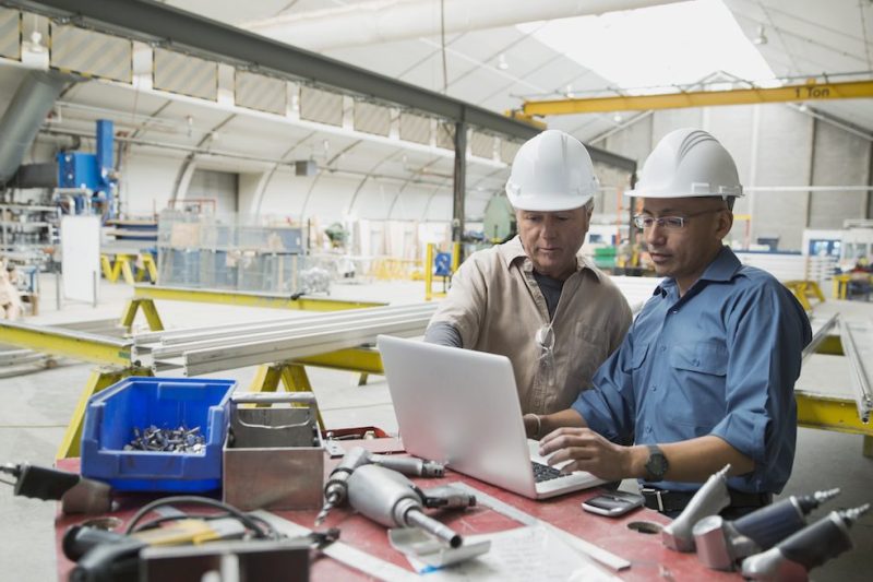 Workers at laptop in manufacturing plant
