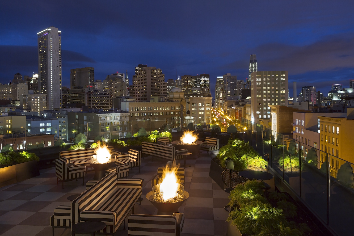 Rooftop seating area with couches, firepits, plants and view of the city