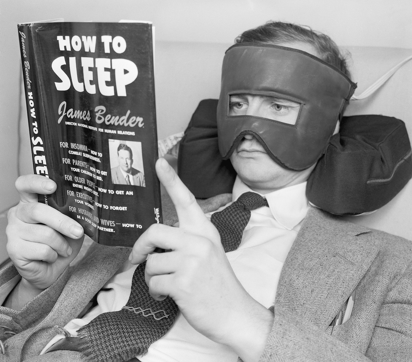 A retailing store of singular distinction is the Lewis & Conger Sleep Shop. An insomniac's paradise, the shop is the only one of its kind in the world, selling items devoted exclusively to wooing comfort in bed and good old sleep. Television comic Wally Cox, who is sometimes troubled with uneasy slumberings (even as you and I), was caught trying out some of the newest bedtime innovations. Photo shows: Wally Cox catches up on some pertinent readings while wearing an electric facial mask that soothes aches and pains with gentle heat. His head rests on a neck pillow that props and supports the head for reading at a good angle.