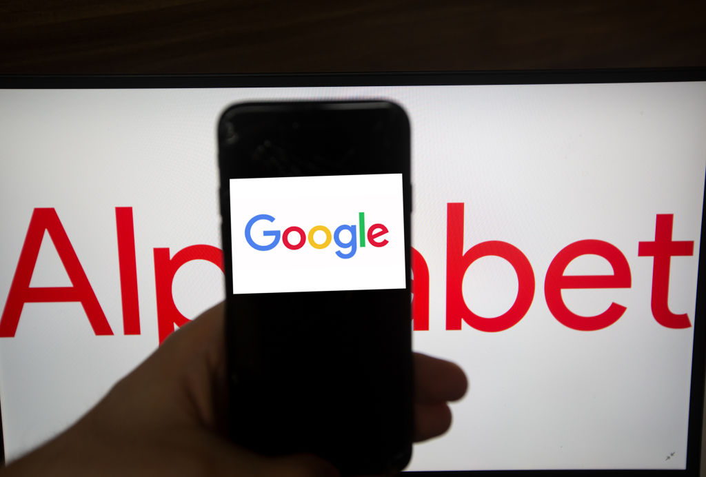 The logo of Google is seen on a screen. In the background there is the logo of Alphabet. Alphabet is the mother company of Google. It has a revenue of 117 billion dollars. (Photo by Alexander Pohl/NurPhoto via Getty Images)