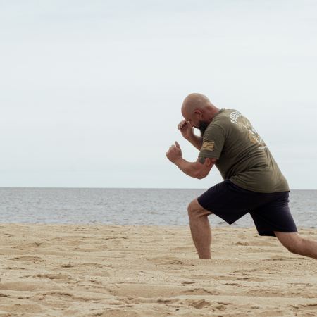 A man doing lunges in the sand while shadow-boxing.