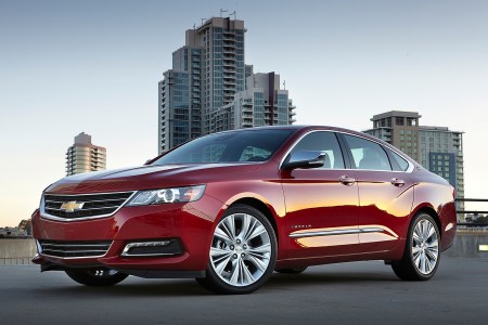 A red sedan in front of city buildings