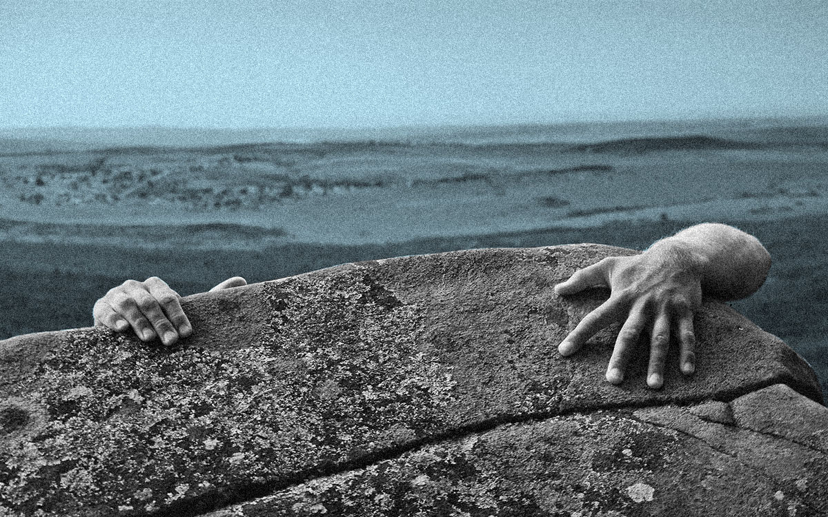 A hand reaching for a climbing hold on a rock wall.