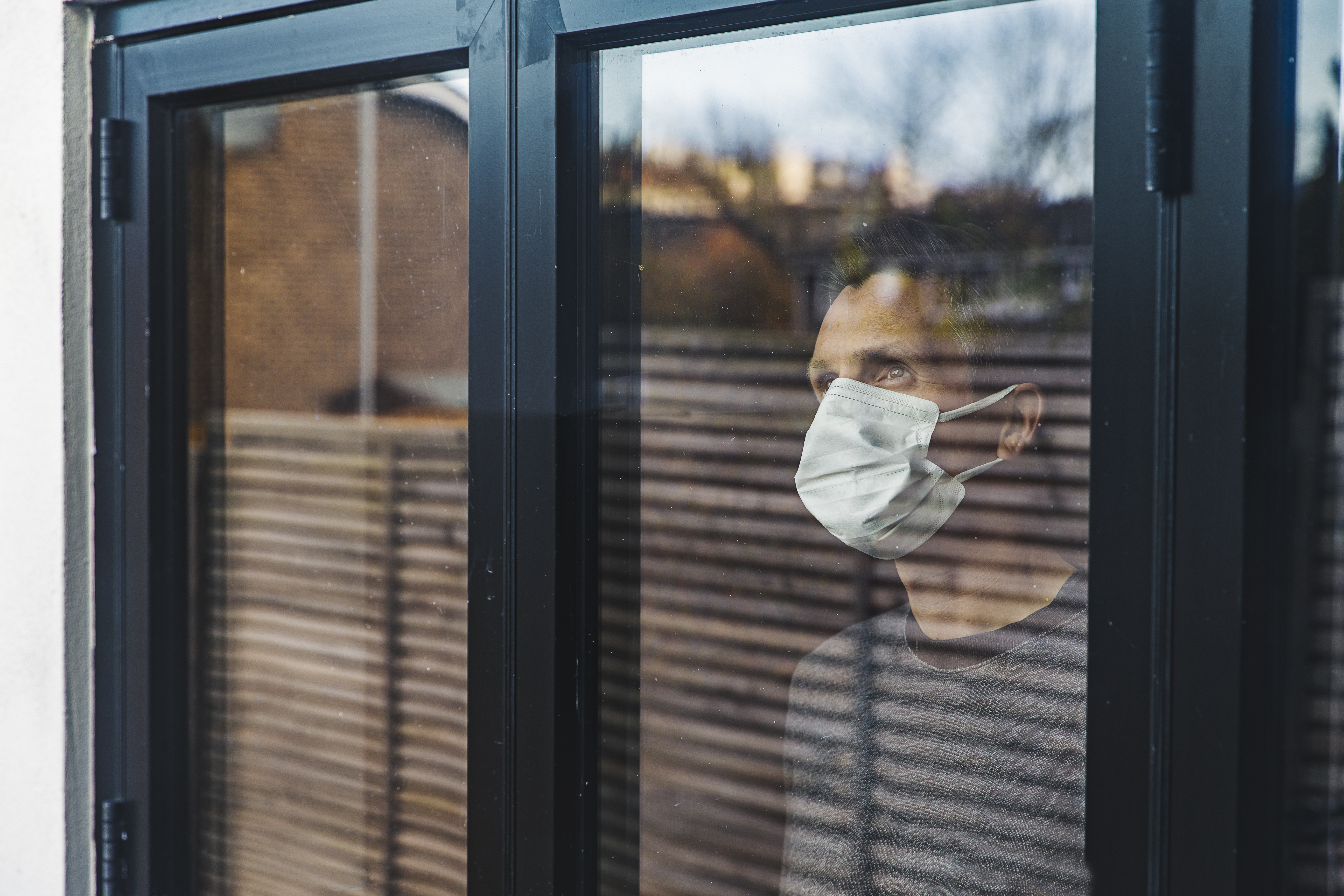 man standing behind glass in a face mask