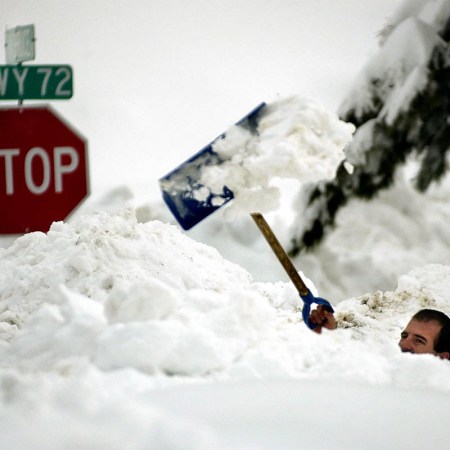 A man tossing snow over his head with a shovel. Here are the best stretches after shoveling snow.