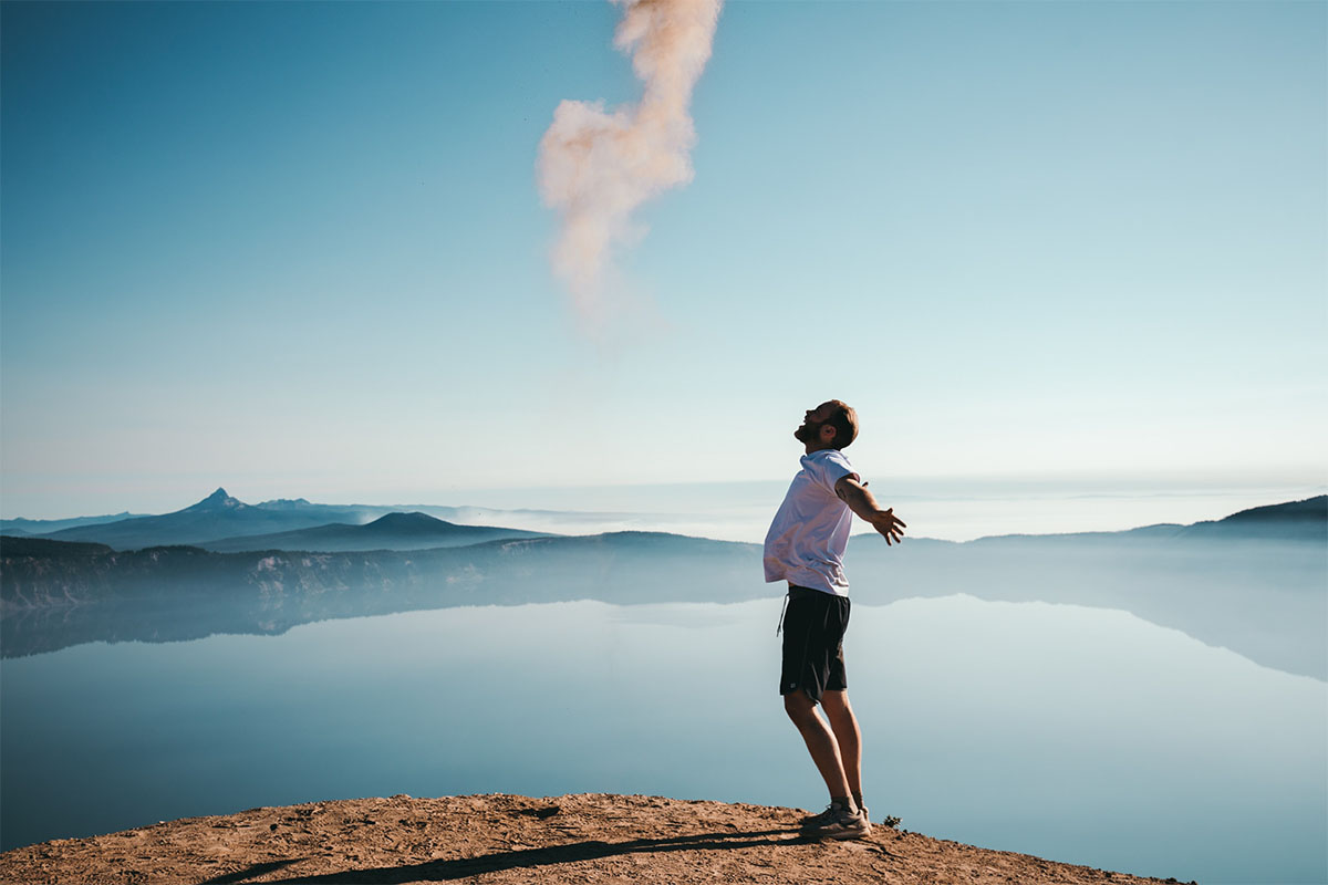 A man on a cliff shouting in joy overlooking a beach, suggesting happiness