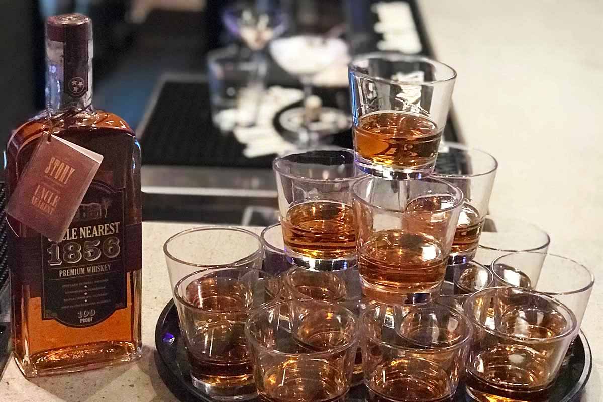 A bottle of Uncle Nearest whiskey next to a tray of glasses filled with the spirit.