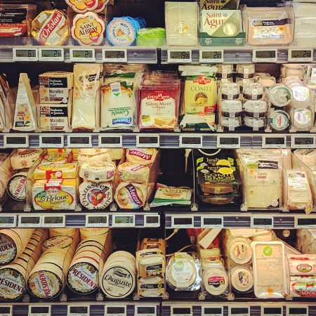 A selection of cheeses at a grocery store on refrigerated shelves