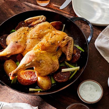 The Smithey Carbon Steel Round Roaster sitting on a table with a chicken and potatoes in it