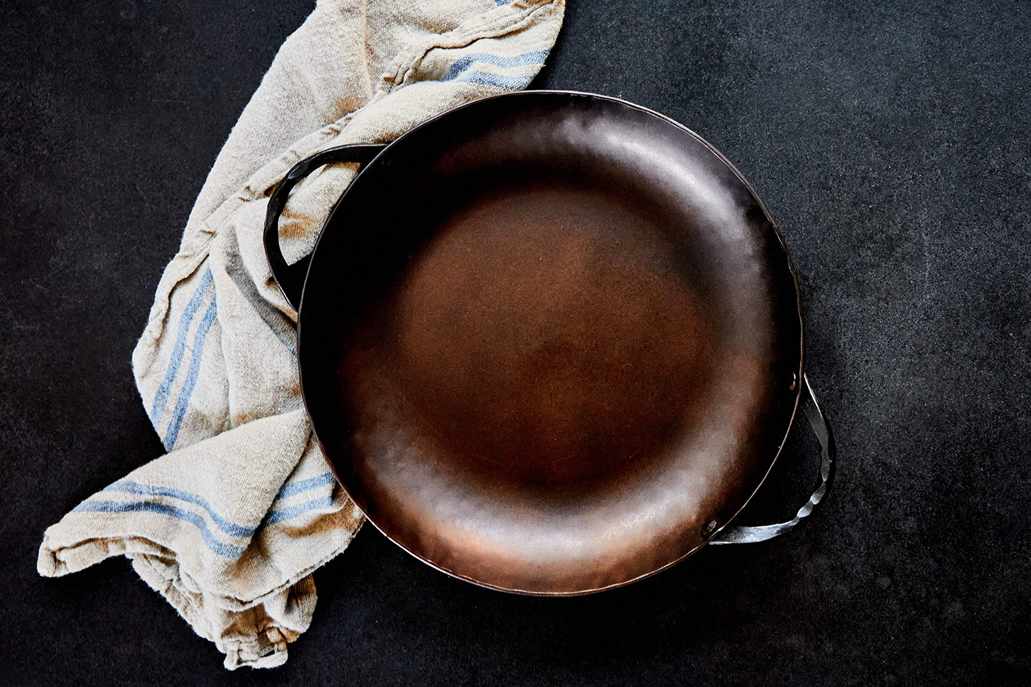 The Smithey Carbon Steel Round Roaster sitting on a table with a chicken and potatoes in it