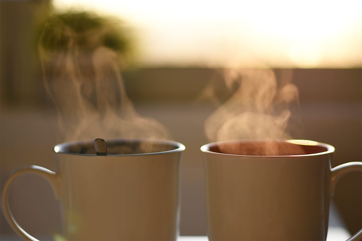 Steam rising off of two cups of coffee with the sunrise in the background
