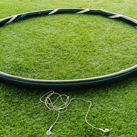 A weighted hula hoop, used for a trendy workout called hooping, sitting in the grass next to earbuds