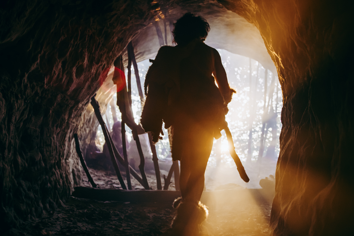 Primeval Caveman in Animal Skin and Fur Holds Stone Tipped Spear Comes out of His Cave into Prehistoric Forest Ready to Hunt. Neanderthal Going Hunting into the Jungle. Shot with Warm Filter.