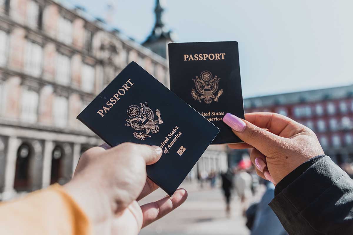 Two people holding out two passports outside. It's taking up to five months to get or renew a passport.