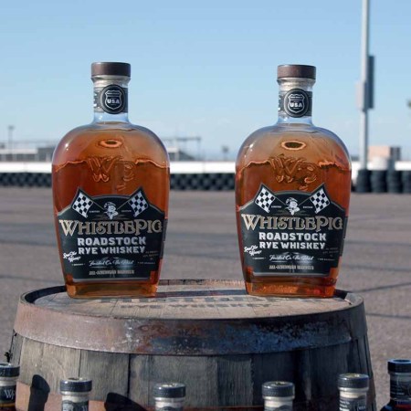 Two bottles of WhistlePig Roadstock Rye Whiskey sitting on a barrel on a track