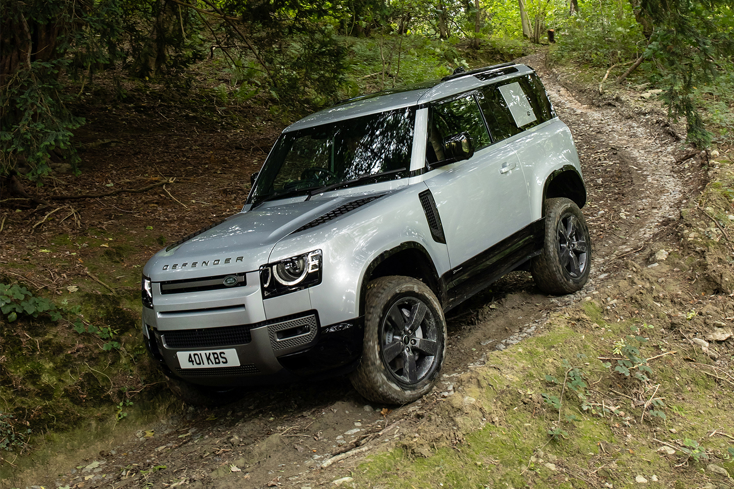 The 2021 Land Rover Defender 90 driving down a trail in the woods. We reviewed the luxury two-door SUV after test driving it in August 2021.