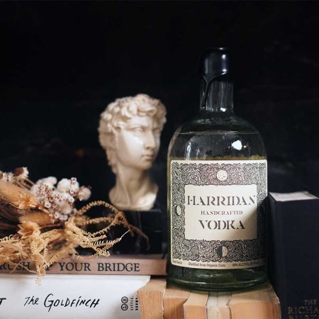 Harridan vodka on a table with various books and artwork — the vodka recently launched with a unique messaging (and real character)