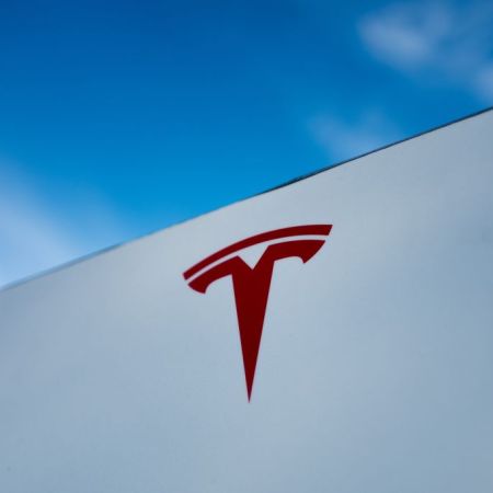 The red Tesla "T" logo on a white building in California. Elon Musk's EV company is under investigation for crashes involving Autopilot and other driver assist features, announced in August 2021.