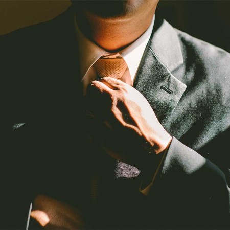 A man in the shadows loosening his tie. A tight tie has been linked to a myriad of health issues.