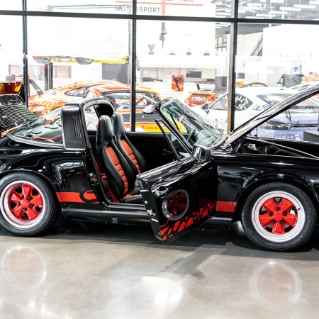 A 1989 Porsche 911 Targa G-Model in red and black restored by Porsche Ontario for the Porsche Classic Restoration Challenge sitting in front of a bunch of other sports cars