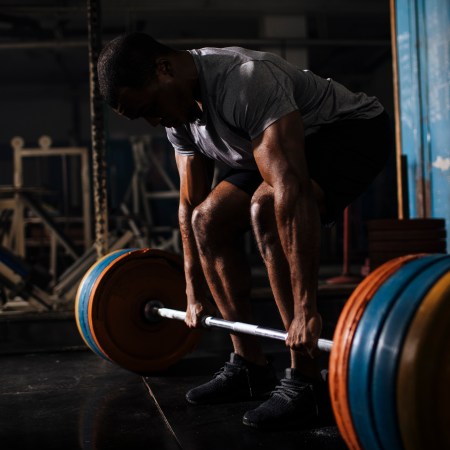 A man lifting a heavy barbell in a darkly lit gym.