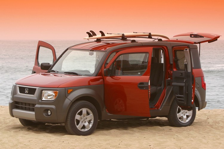 An orange and brown Honda Element SUV with all the doors open and a surfboard on top sitting on the beach at sunset