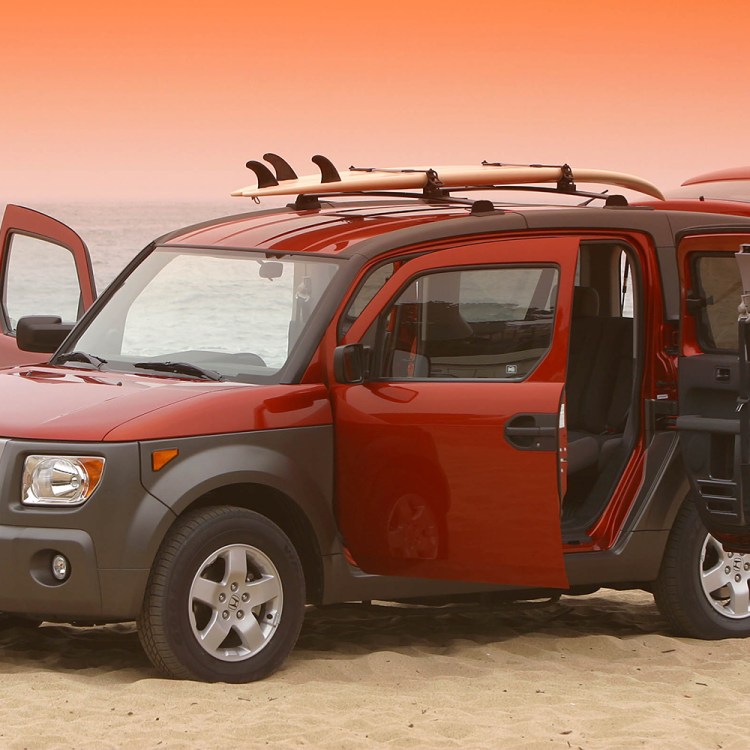 An orange and brown Honda Element SUV with all the doors open and a surfboard on top sitting on the beach at sunset