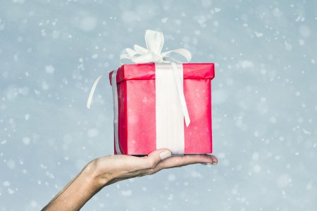 A woman's hand holding a red-wrapped gift with a white ribbon