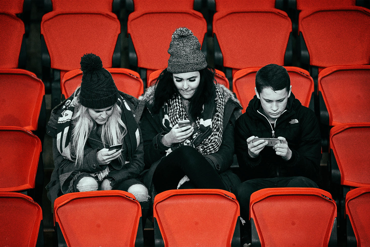 Three young people in the stands at a professional soccer game browse their smarthpones