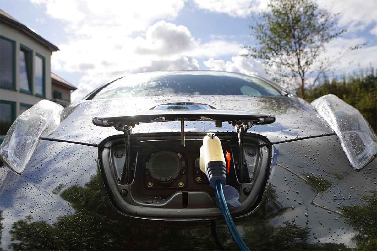 Electric car being charged outside home. New homes and businesses will need ports for charging EVs starting next year in the UK.