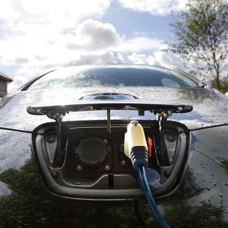 Electric car being charged outside home. New homes and businesses will need ports for charging EVs starting next year in the UK.