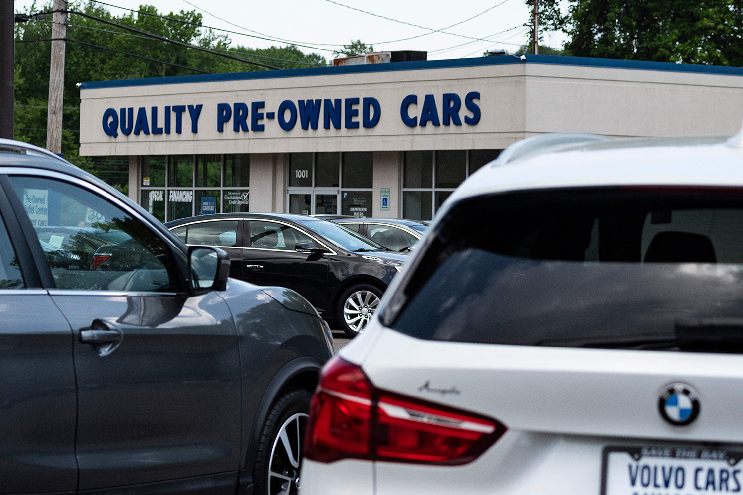 A white BMW seen in the foreground of a photo of a used car dealership lot in Annapolis, Maryland on May 27, 2021