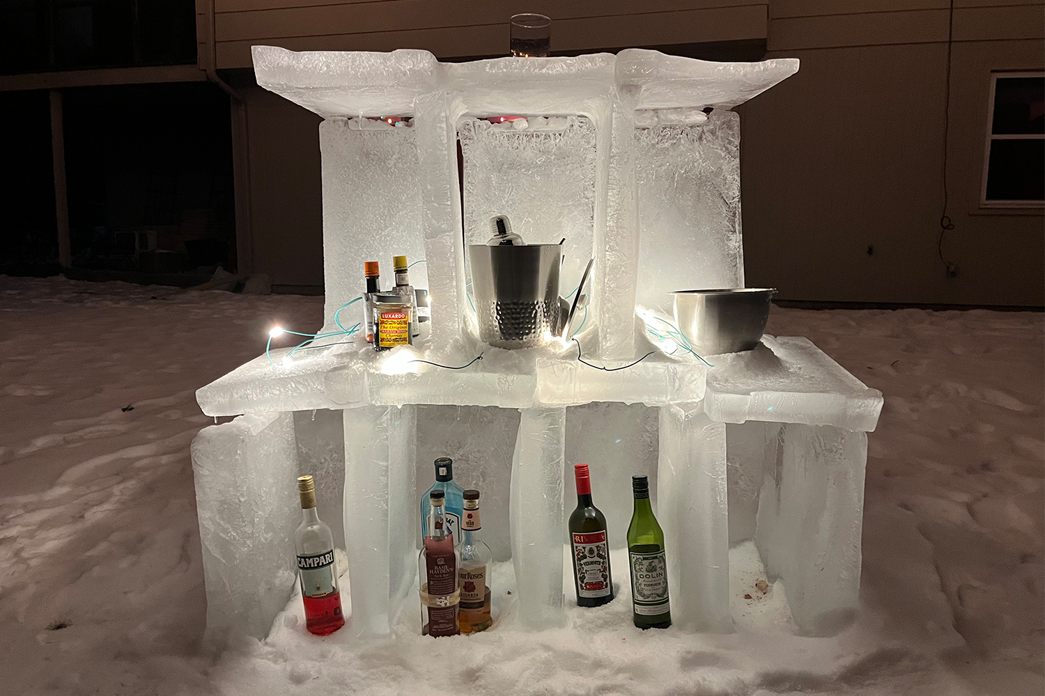 Behind an ice bar in the backyard of a home, with bottles of booze, liqueurs, bitters and other cocktail fixings