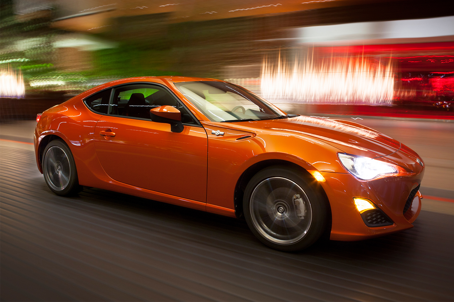 The 2013 Scion FR-S sports car in orange driving at night 