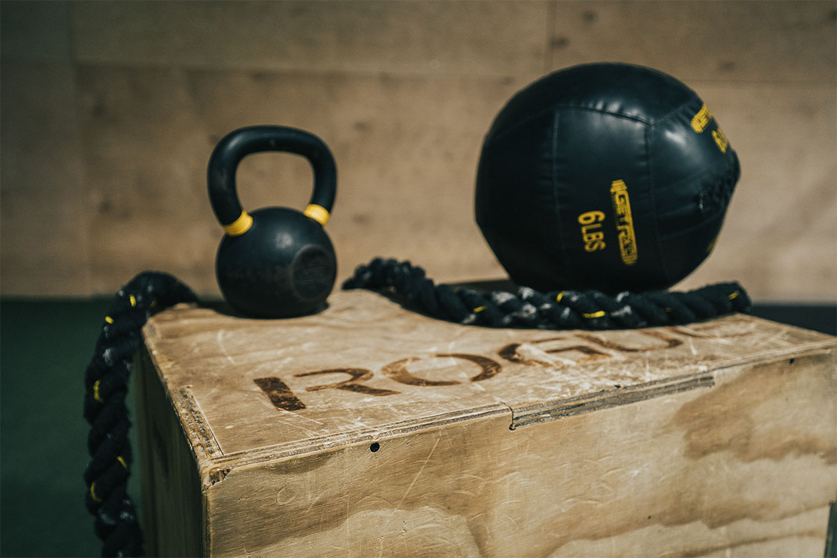 A man in a gym lifting a barbell with a kettlebell attached. This is what's known as chaos training.