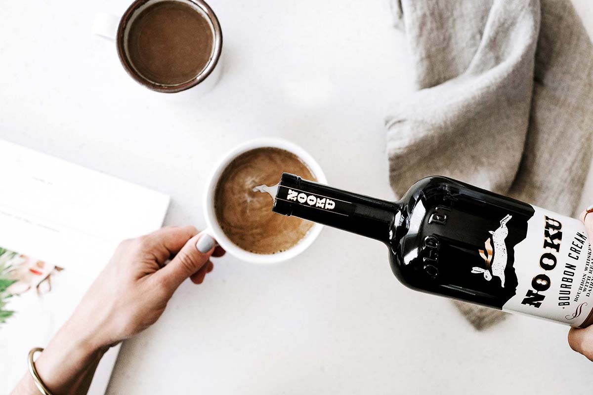 a person pouring Nooku bourbon cream into a cup of coffee