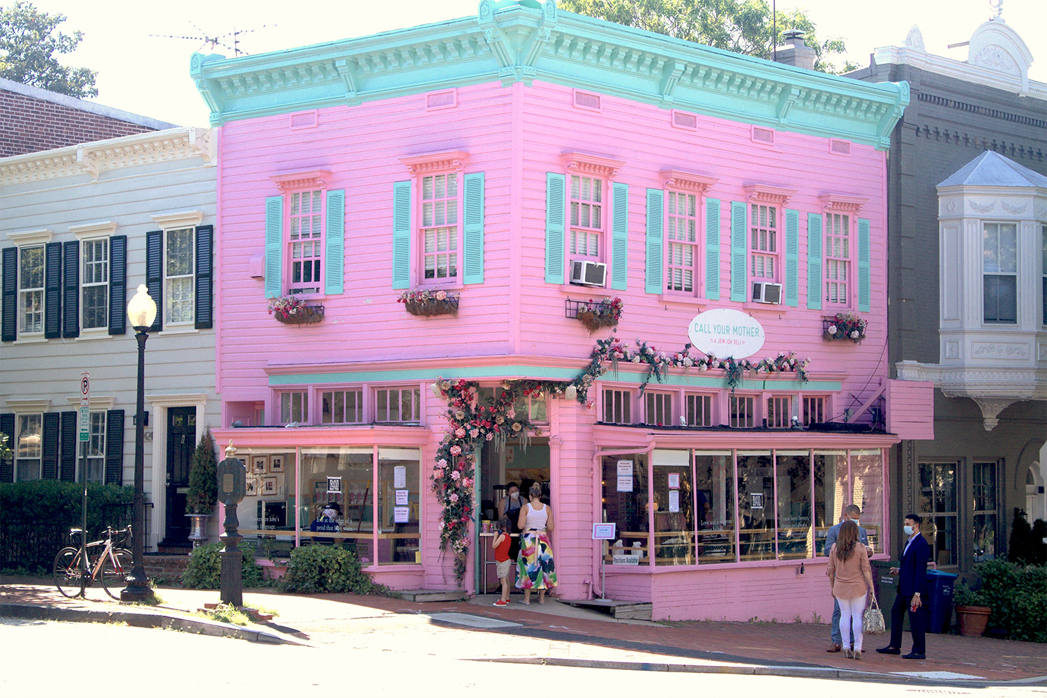 Exterior of Call Your Mother's pink and blue storefront, door framed with flowers.