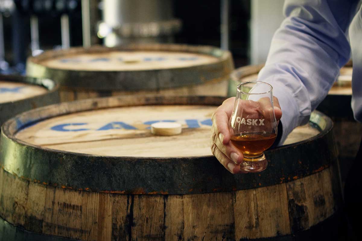 A whiskey glass and whiskey barrel stamped with CaskX, a whiskey investment firm