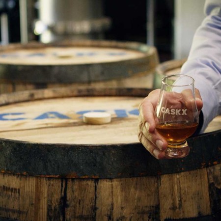 A whiskey glass and whiskey barrel stamped with CaskX, a whiskey investment firm