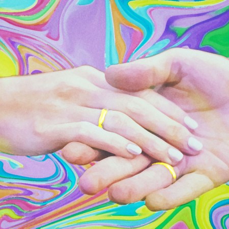 Hands with wedding rings clasped against a colorful background