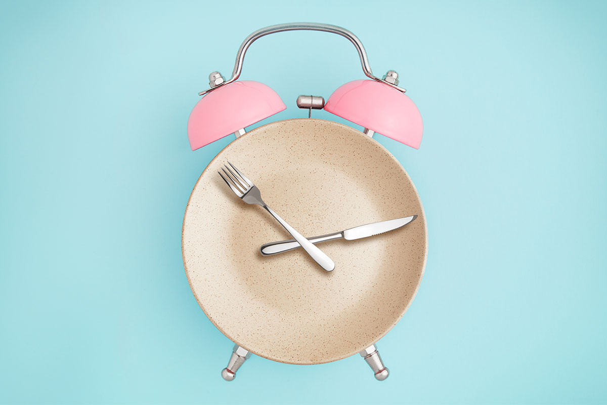 A fork and knife arranged as clock hands on an alarm clock. A new study shows that intermittent fasting doesn't provide any unique benfits.